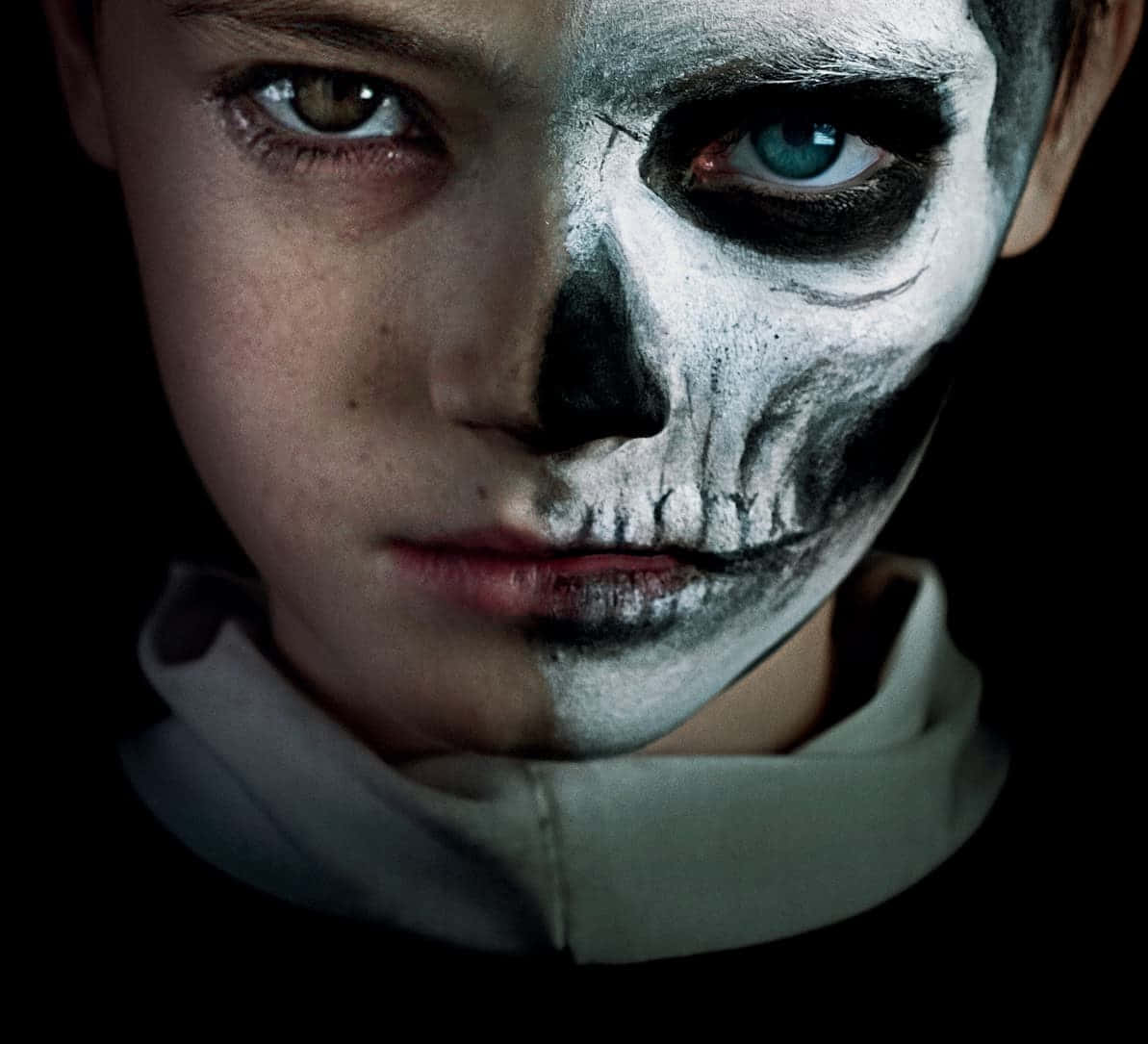En ung dreng med et skelets ansigt malet på hans ansigt stirrer ud fra et lys gul baggrund.