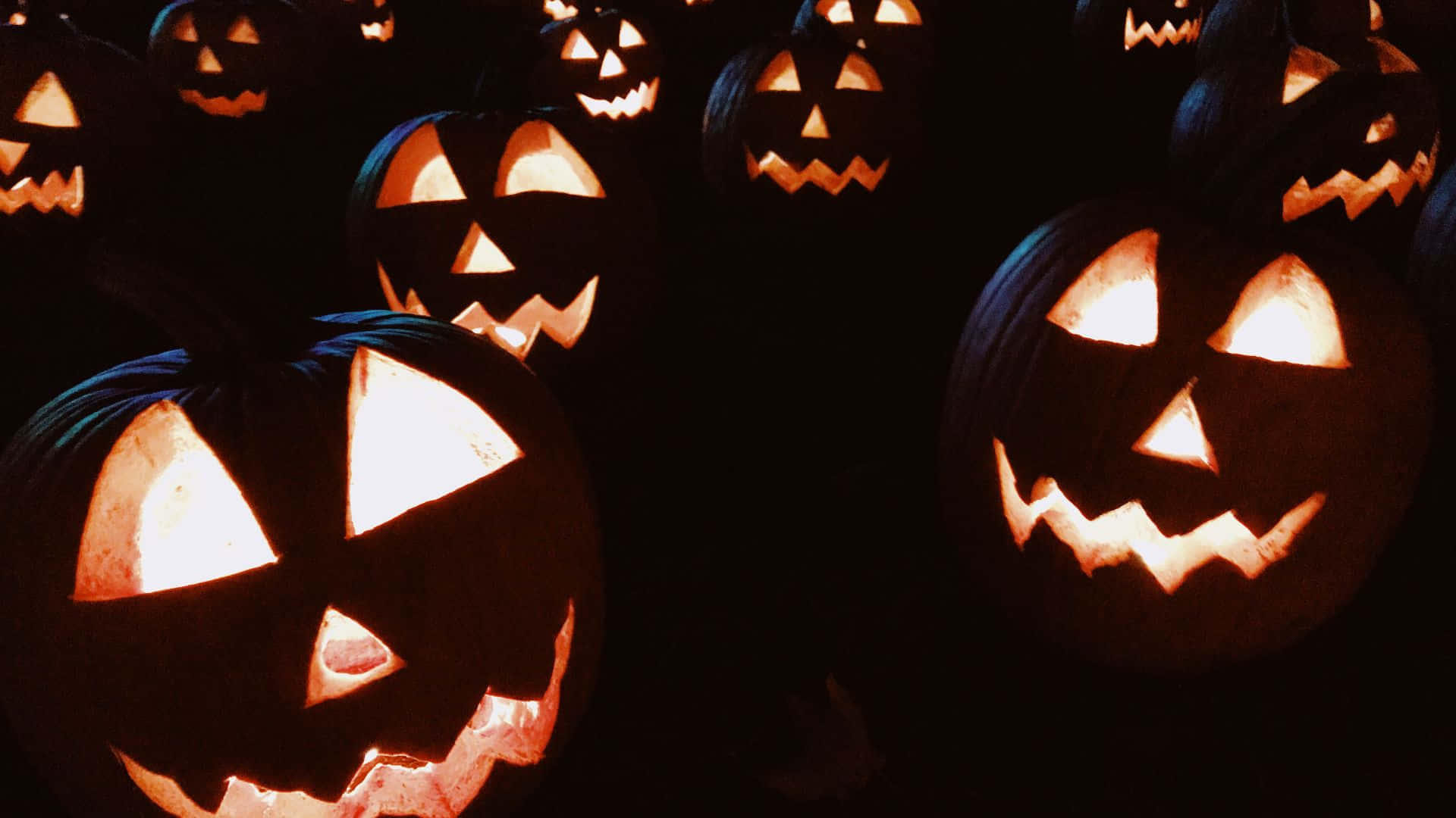 A Group Of Pumpkins With Faces Lit Up In The Dark