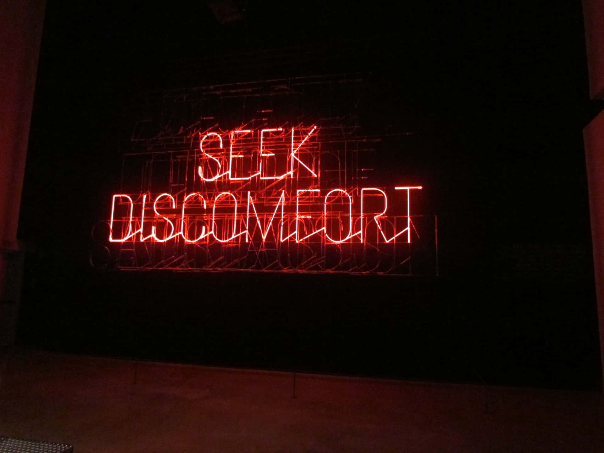 Seek Discomfort, A Neon Sign In A Dark Room Wallpaper