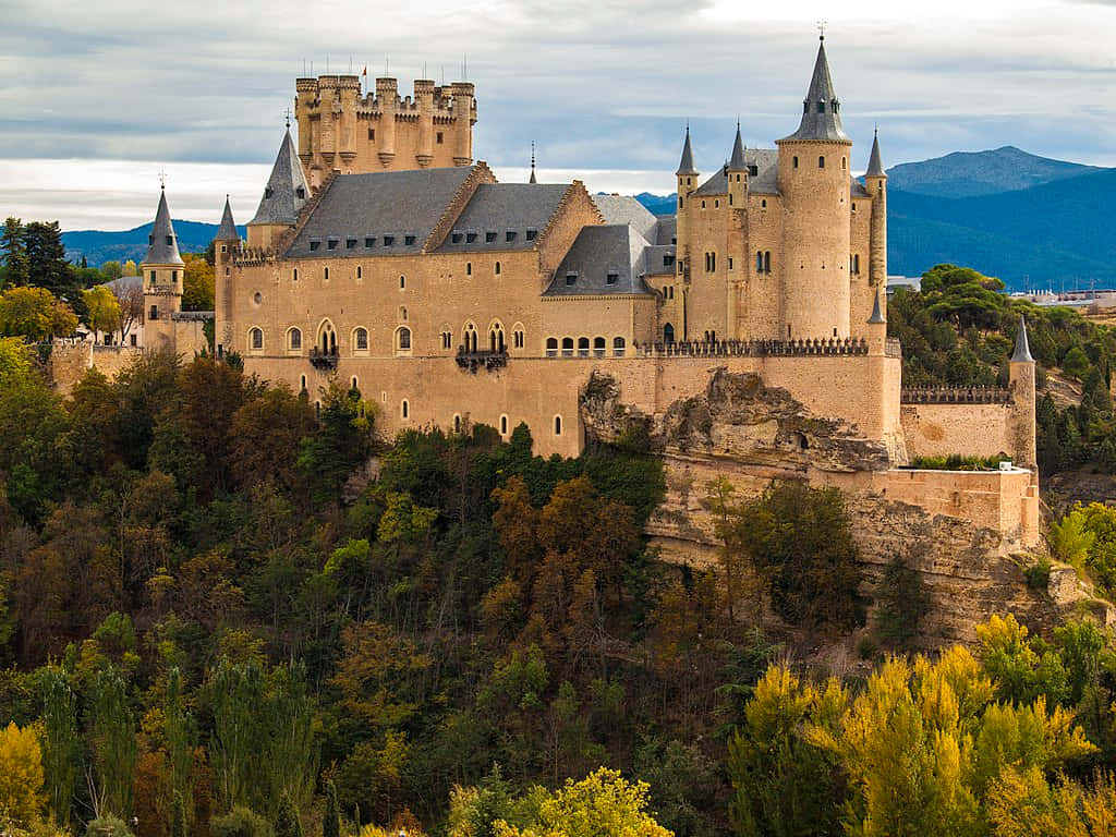 Segovia Castle Overlooking Trees And Mountains Wallpaper