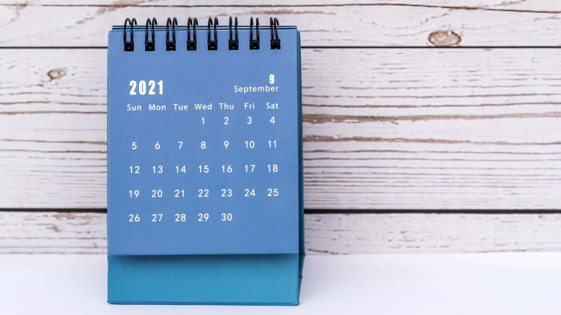 En blå kalender med en sort dæksel på et træbord Wallpaper