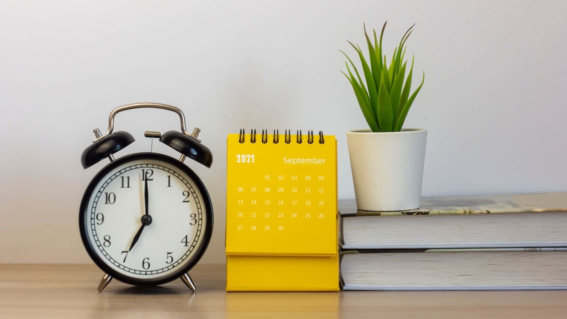 A Yellow Alarm Clock Sits Next To A Book And Plant Wallpaper