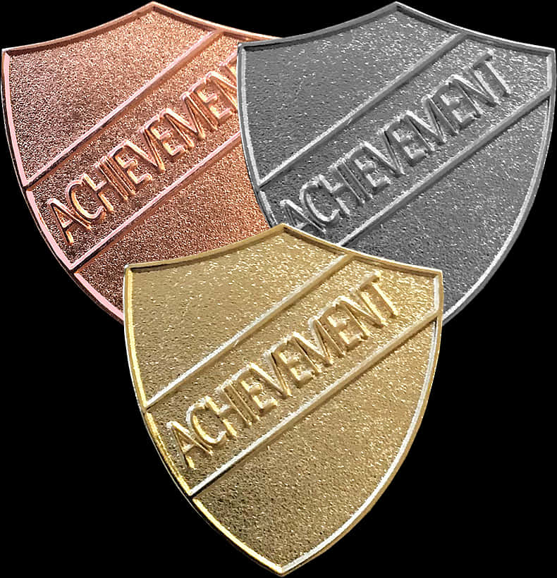 Achievement Shield Trio PNG — Three metallic shield-shaped achievement medals in gold silver and bronze with engraved text against a black background.