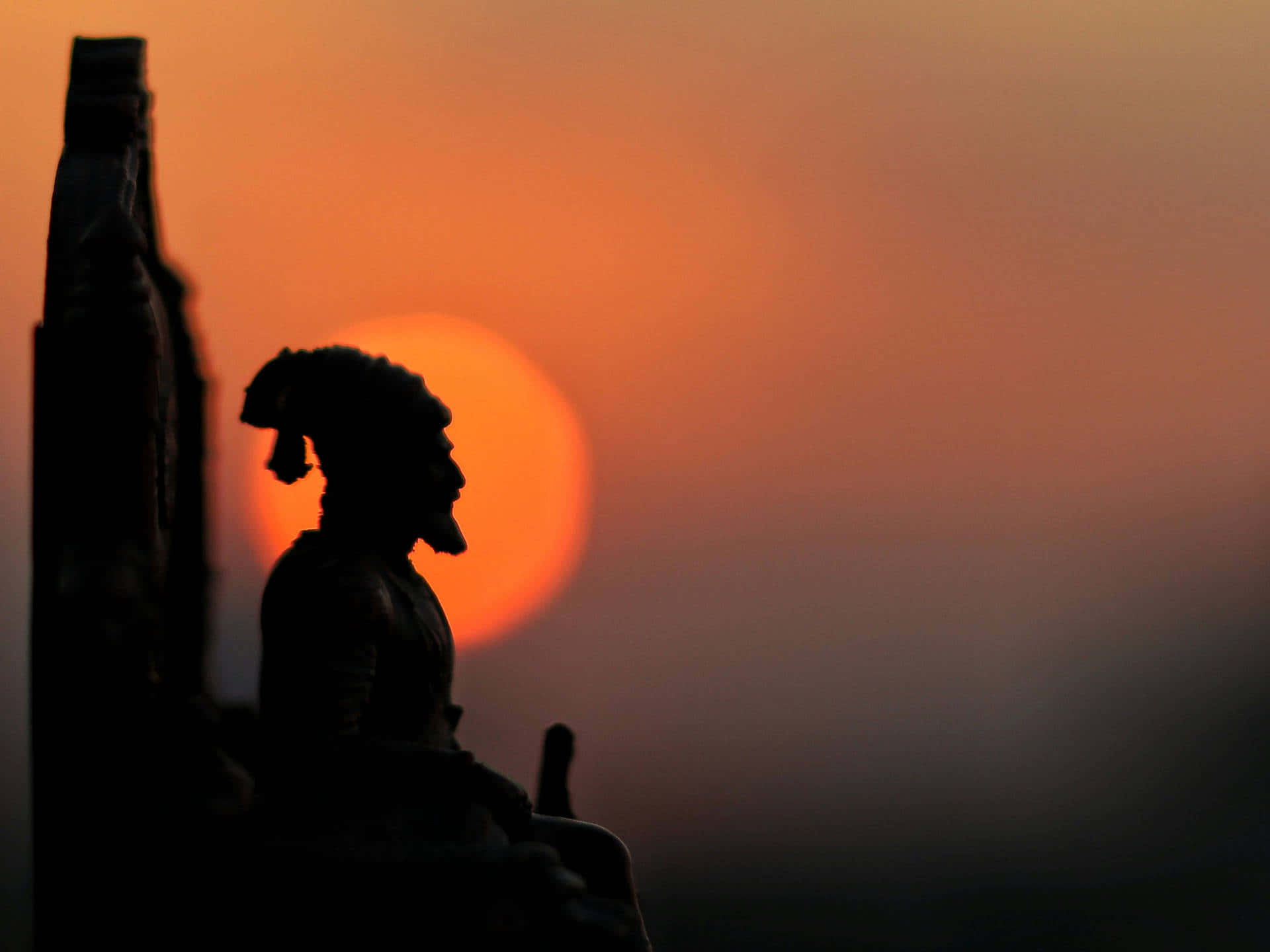 A Statue Of A Man Sitting In Front Of A Sunset