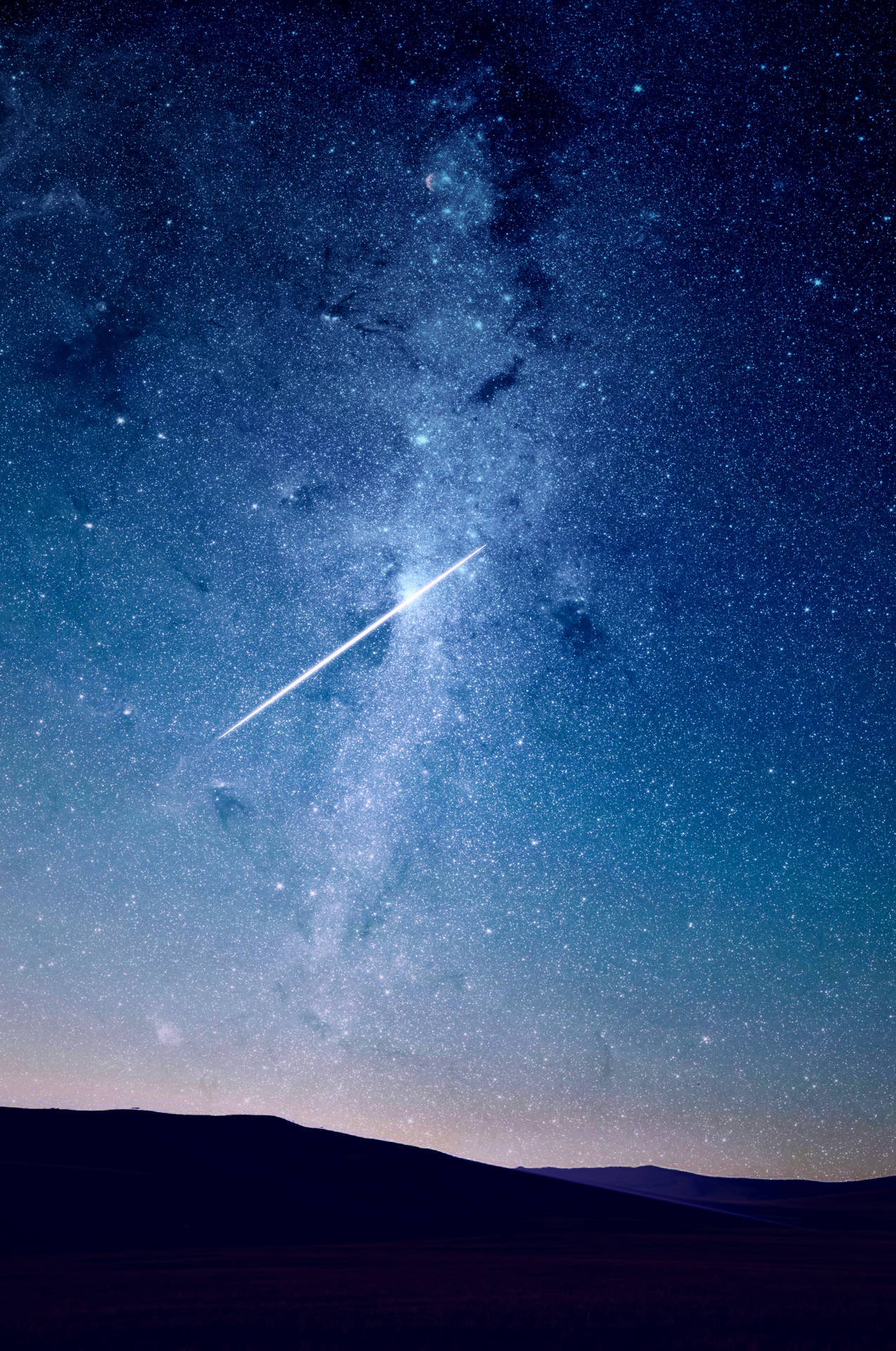Shooting star with white tail on the blue night sky filled with glowing stars of different sizes. 