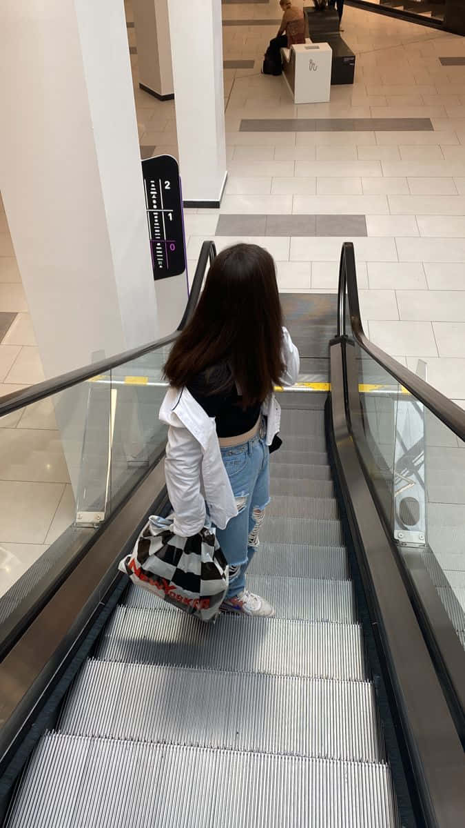 A Woman Is Walking Down An Escalator In A Mall