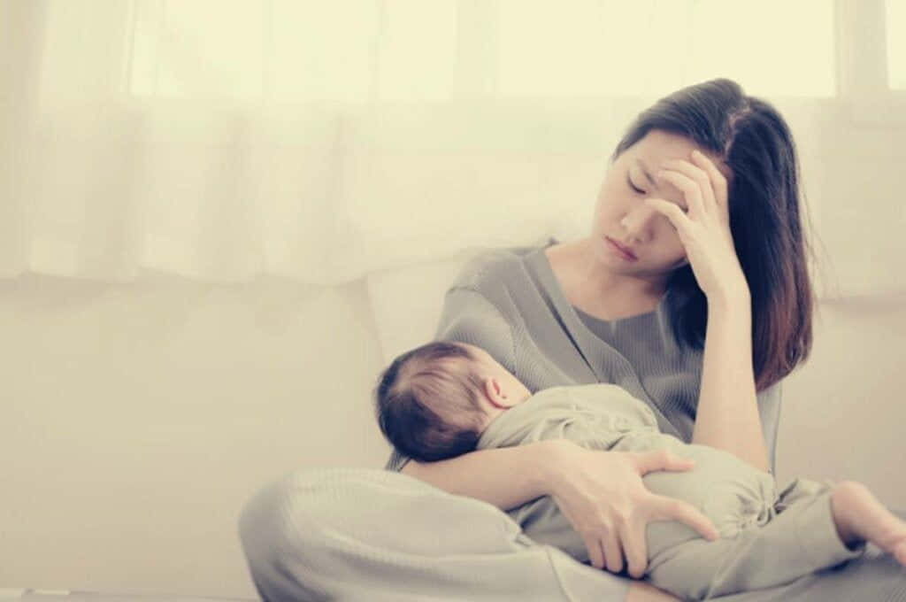 Einefrau Hält Ihr Baby Im Arm Und Hält Sich Gleichzeitig Den Kopf.