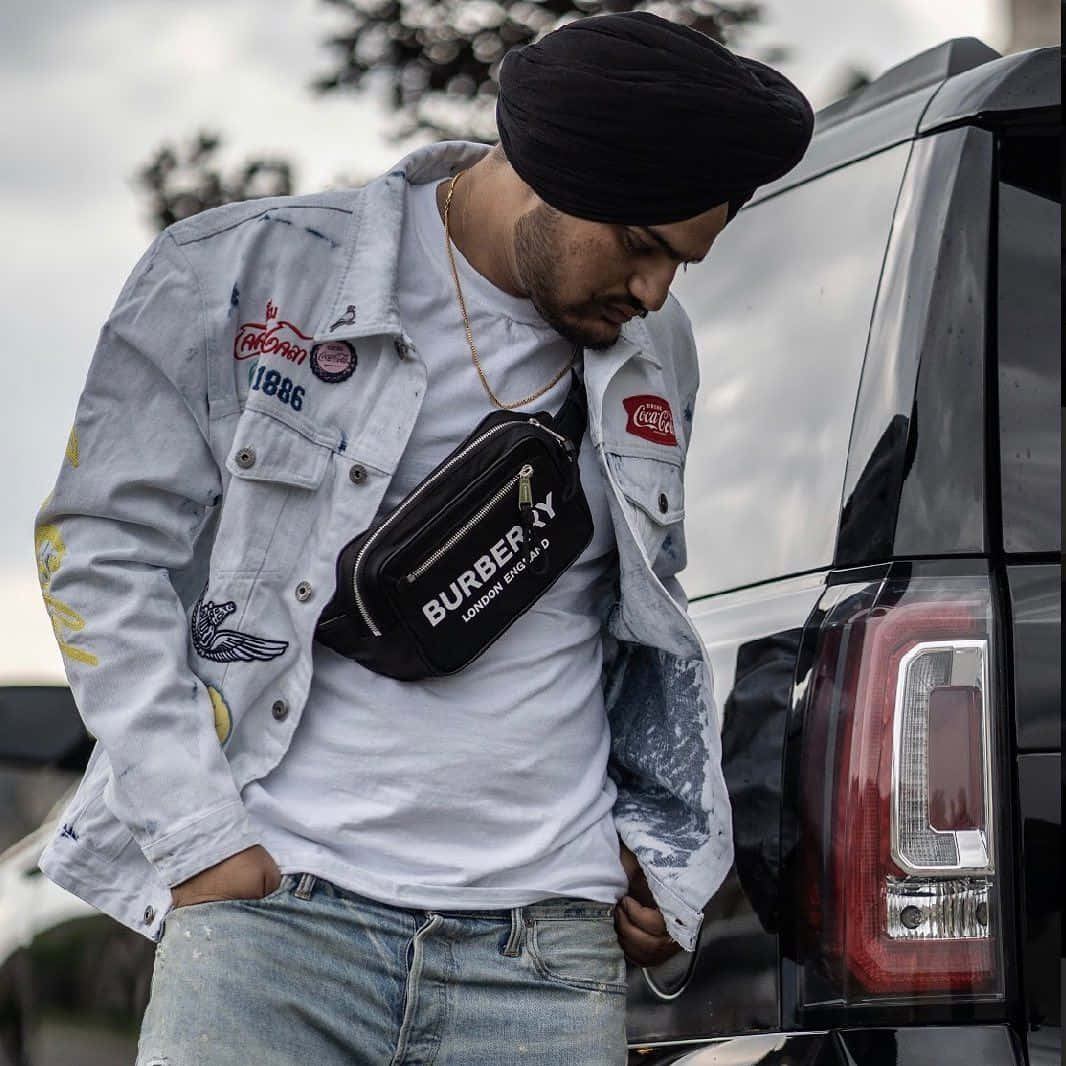 A Man Wearing A Turban And Jeans Standing Next To A Car