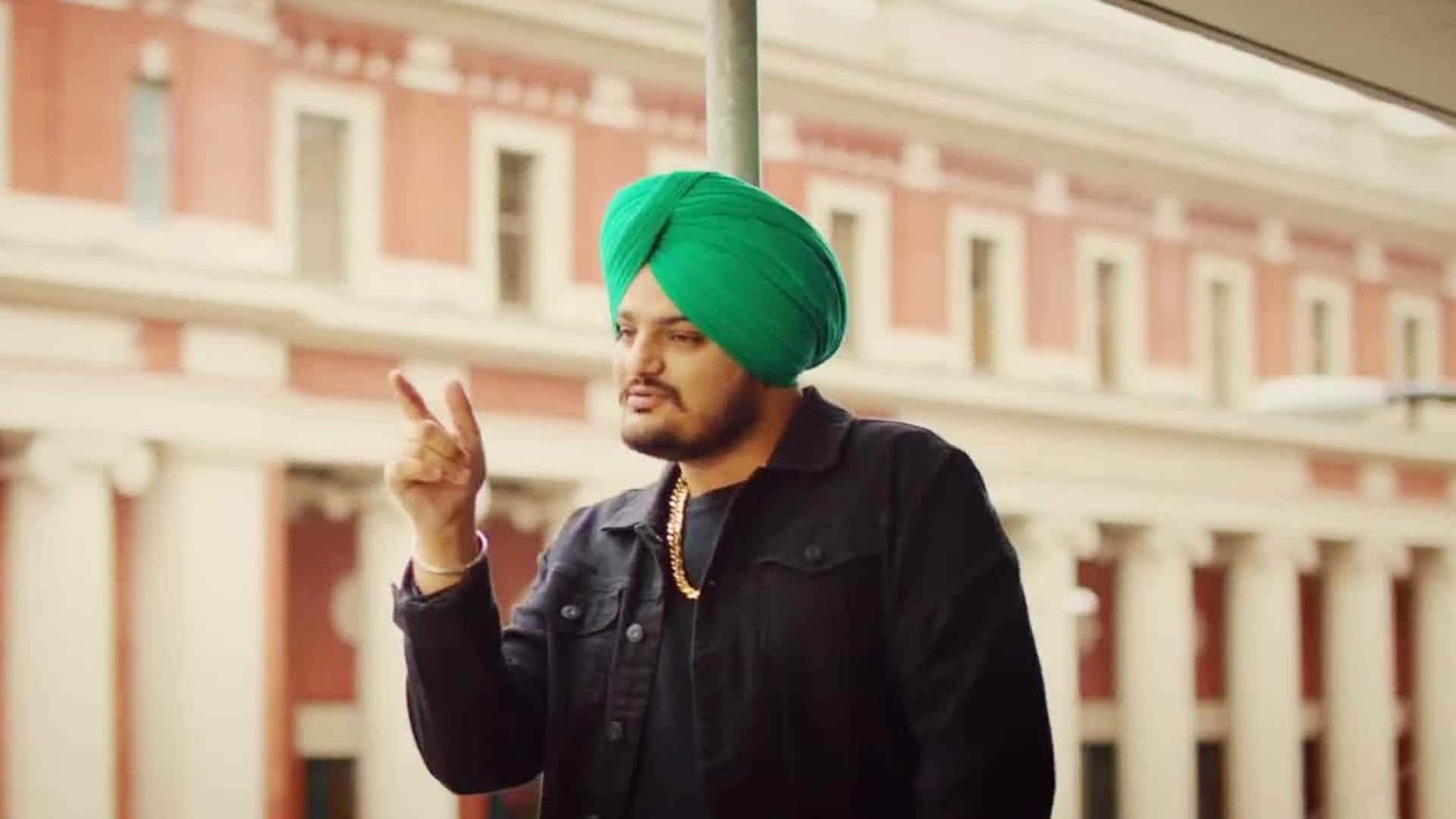 A Man In A Green Turban Is Pointing At A Building