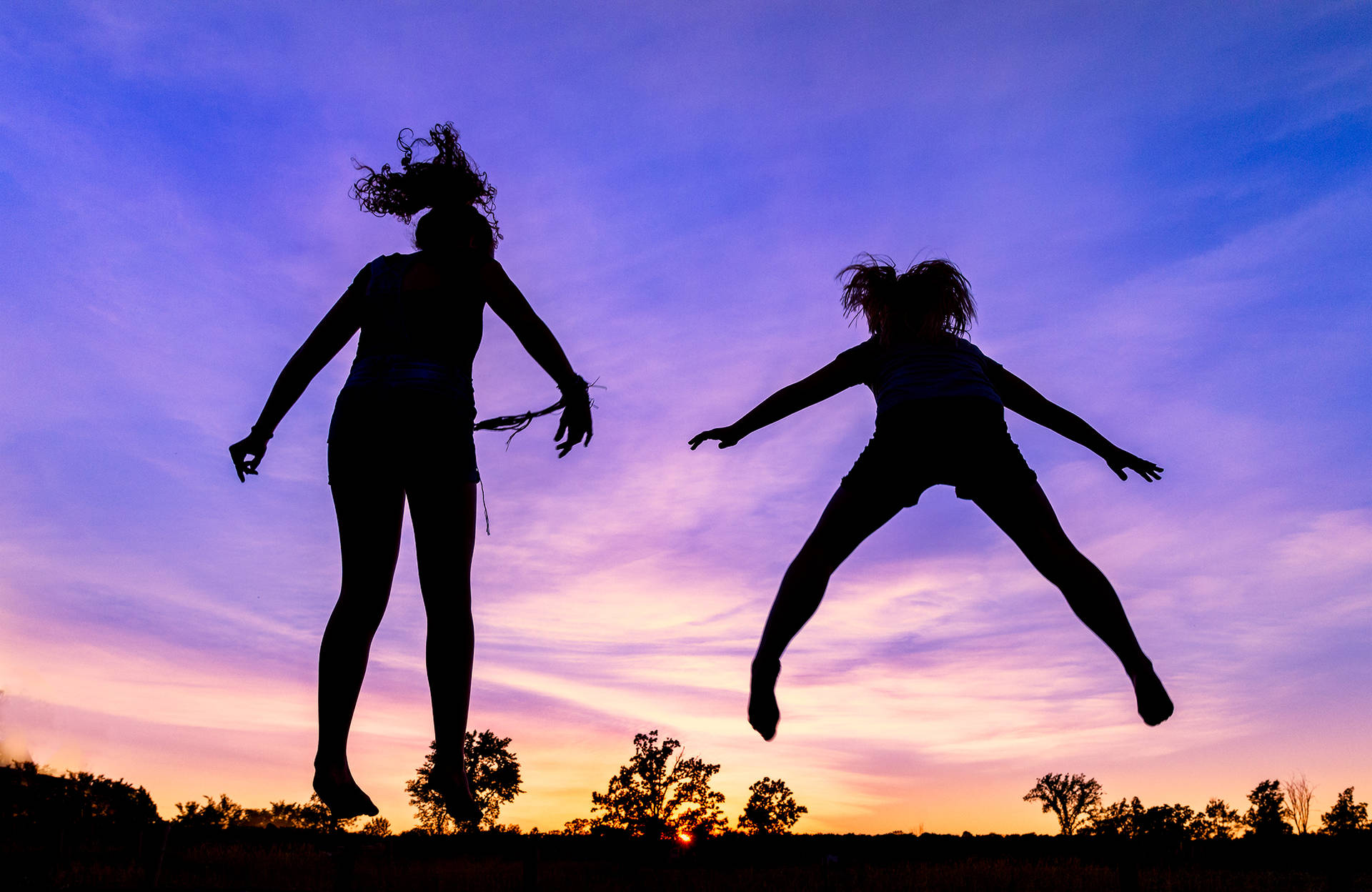 Silhuetterede piger hopper fra en trampolin Wallpaper
