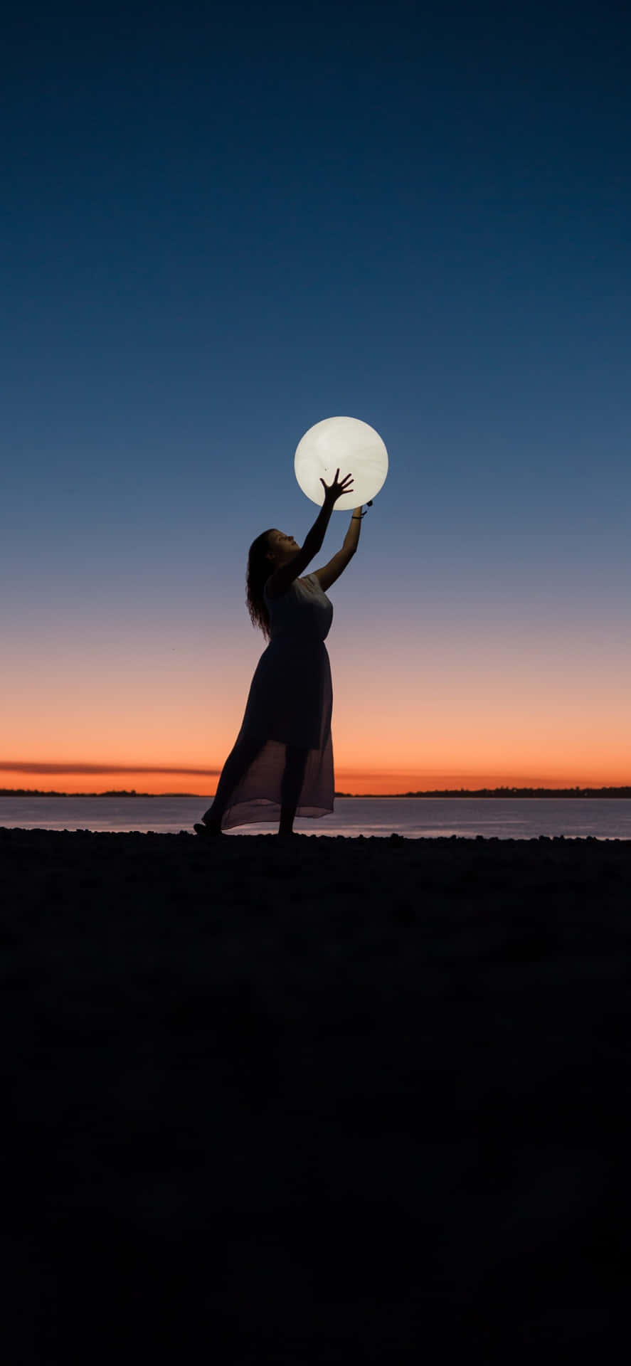 Silhouetteof Woman Holding Moonat Beach Dusk Wallpaper