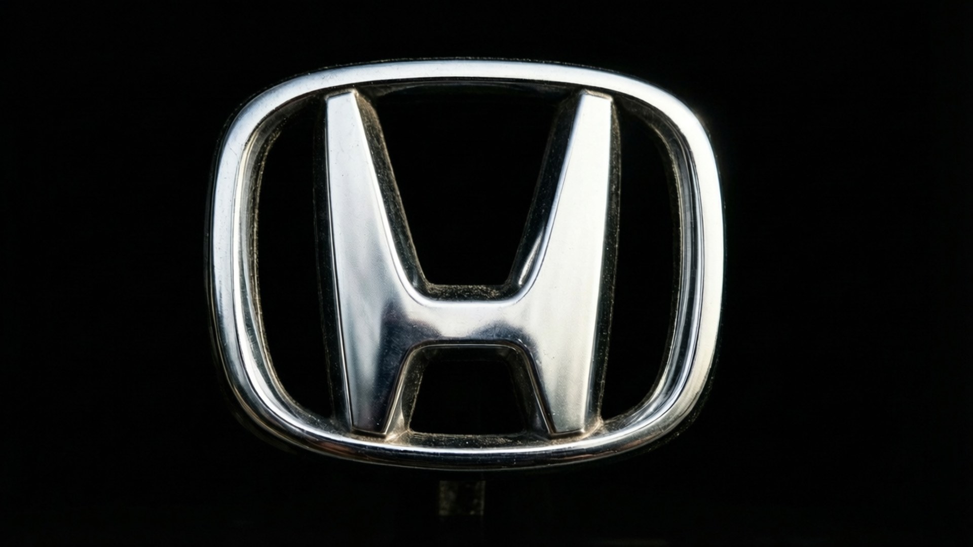 Klassiek zilveren Honda-logo met dramatische schaduwen op zwart.