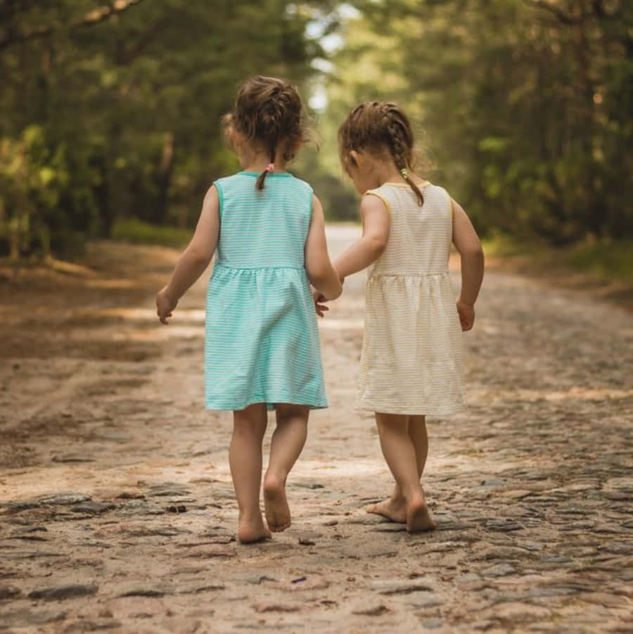 Two Little Girls Walking Down A Road In The Forest