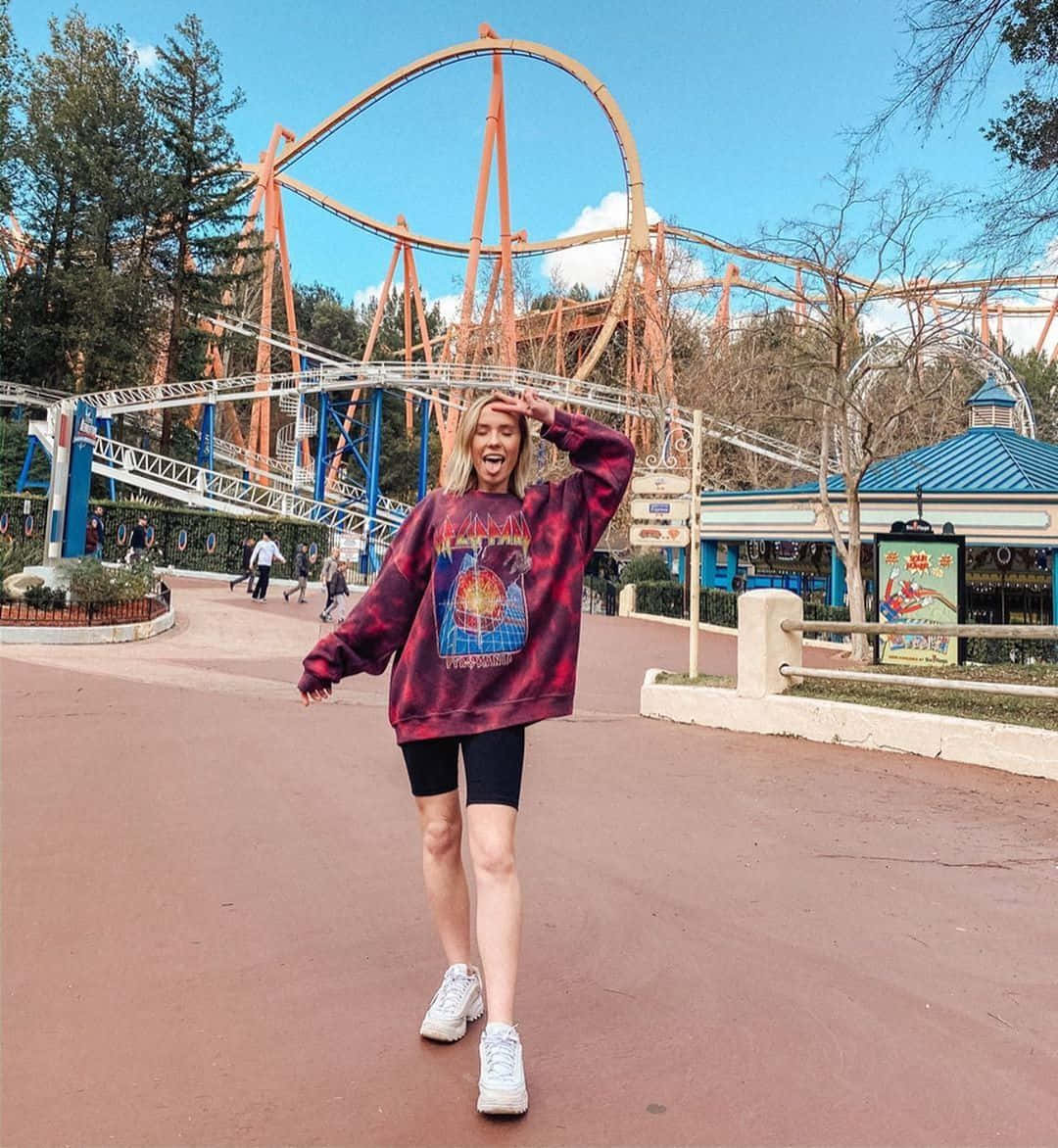 A Woman Standing In Front Of A Roller Coaster