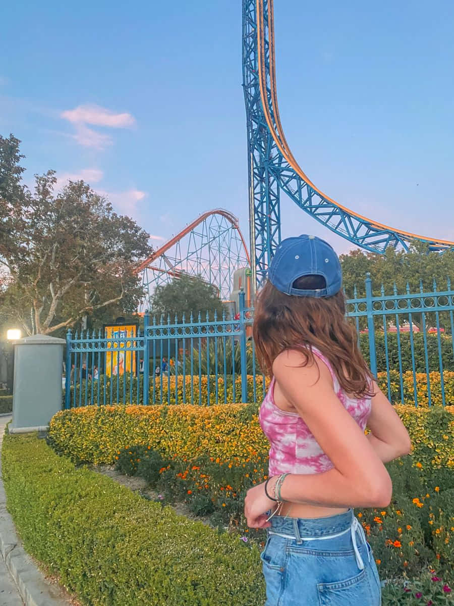 A Girl Standing In Front Of A Roller Coaster