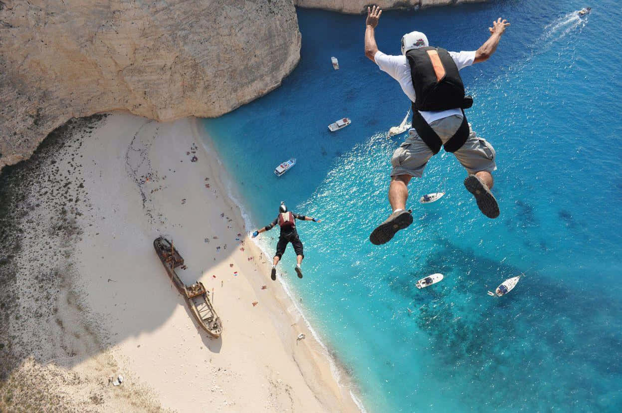 A Man Is Jumping Off A Cliff Near A Beach