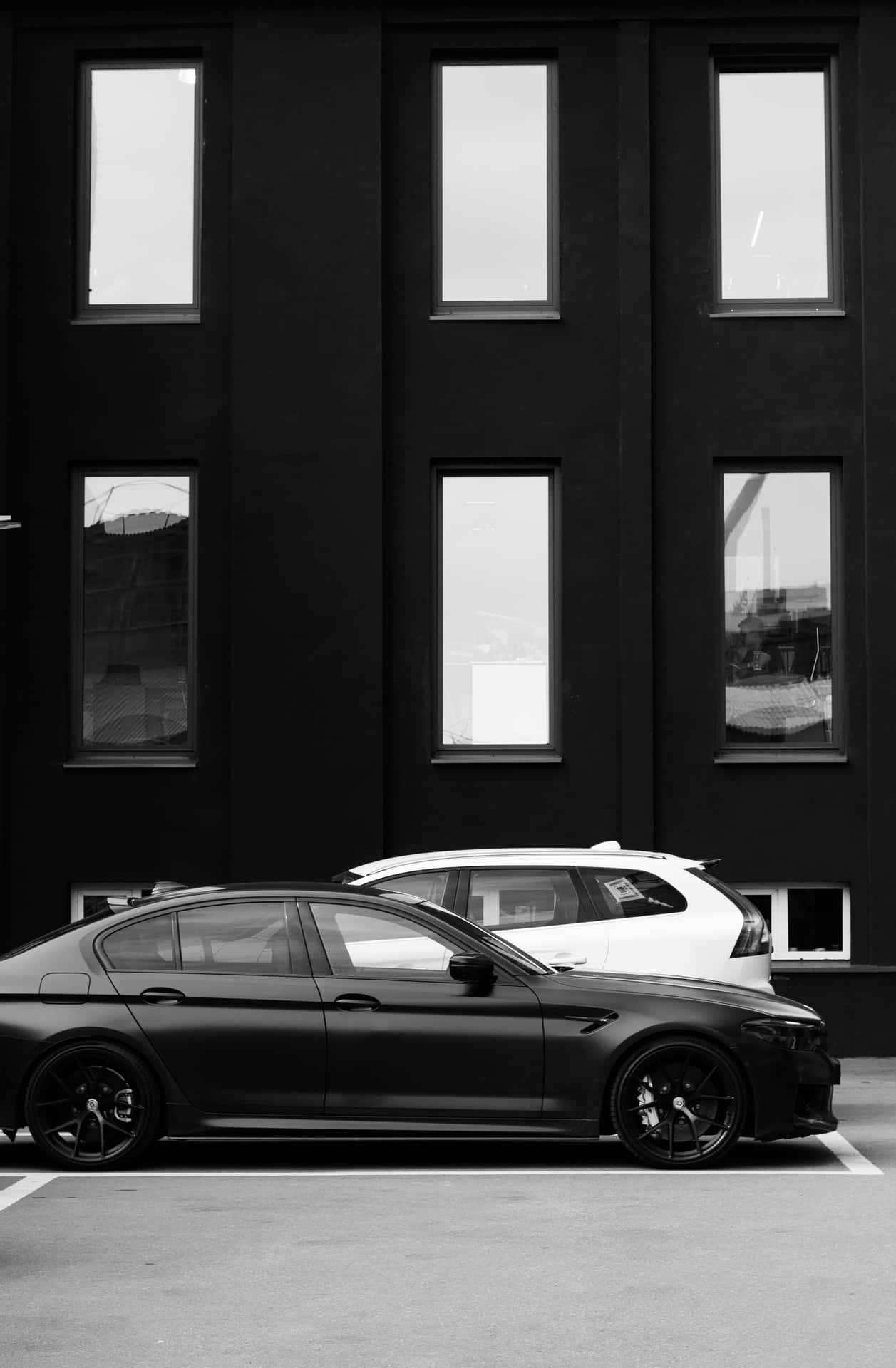 Sleek_ Black_ Car_ Against_ Modern_ Building Wallpaper