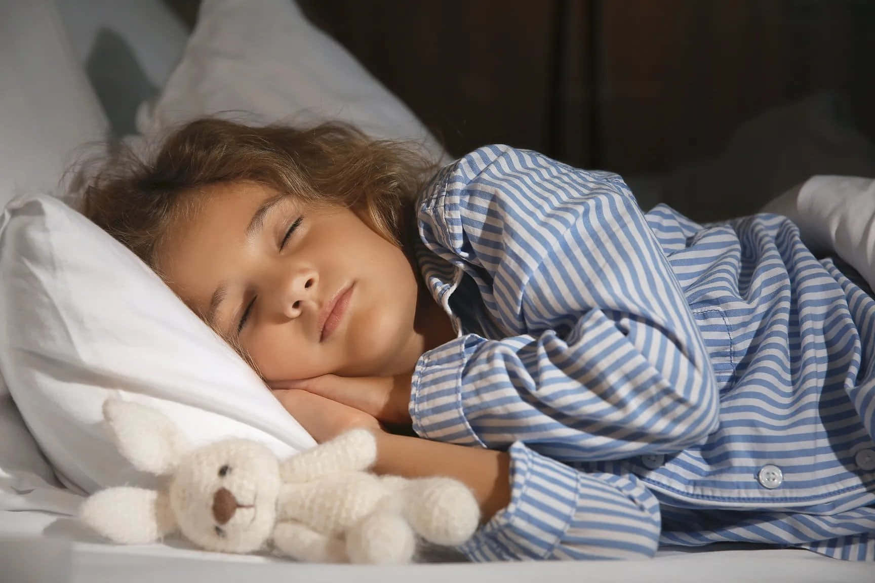 A Young Girl Sleeping In Bed With A Stuffed Animal
