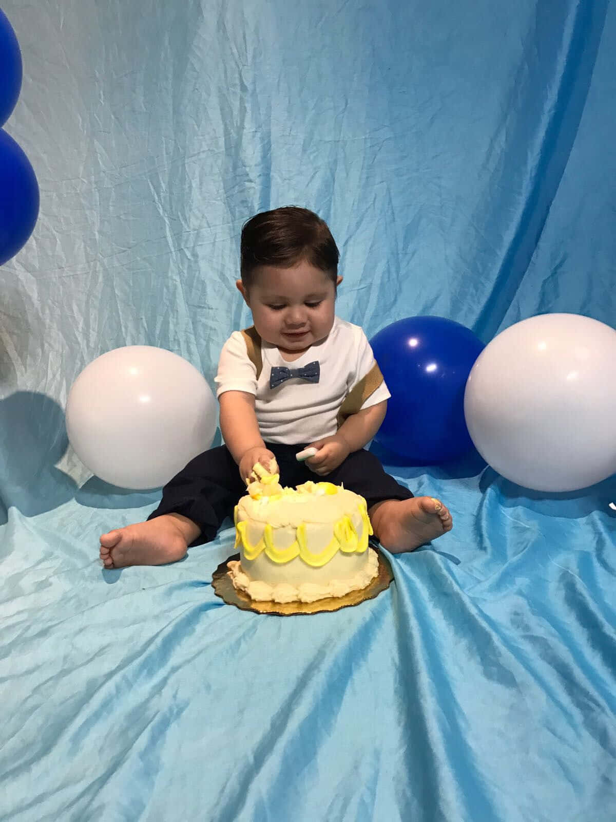 A Baby Boy Sitting In Front Of A Cake With Balloons