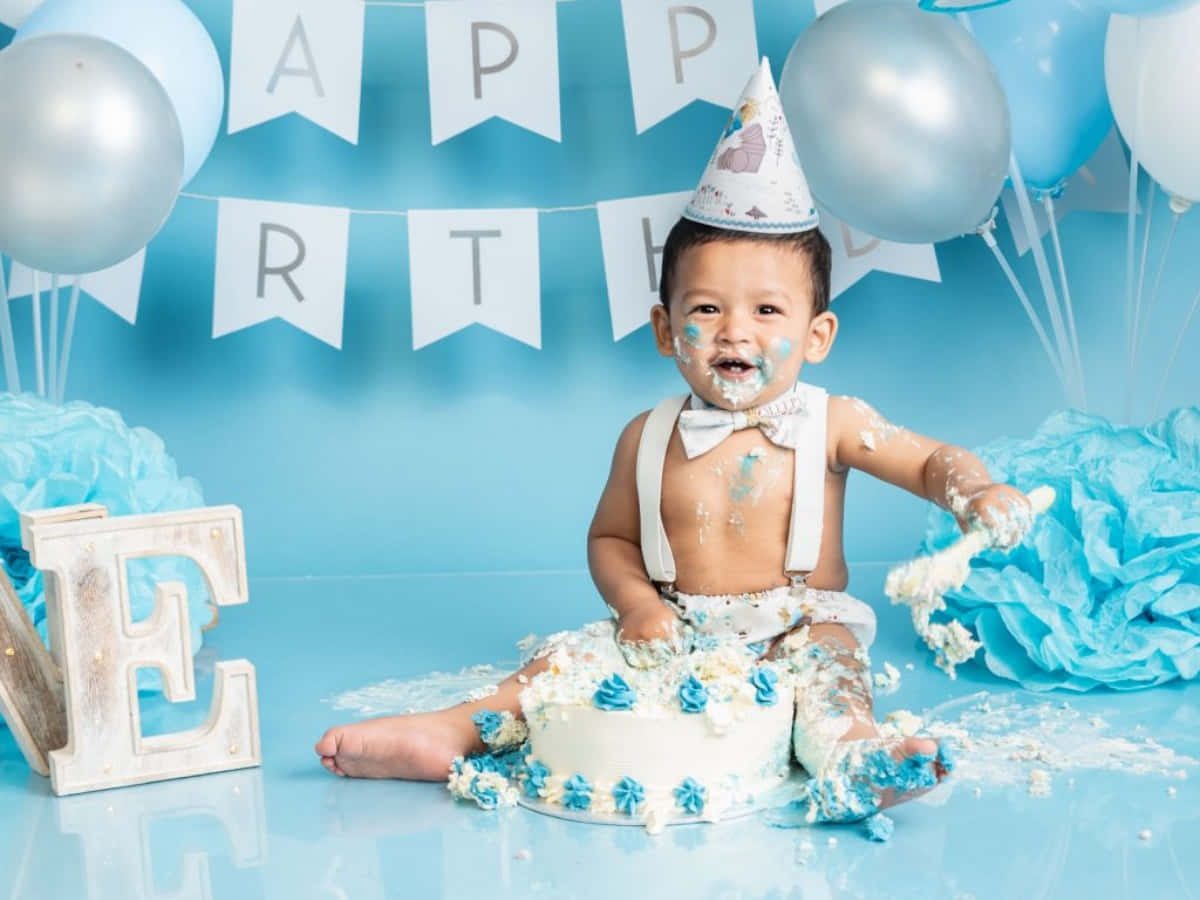 A Baby Boy Is Sitting In Front Of A Cake With Balloons