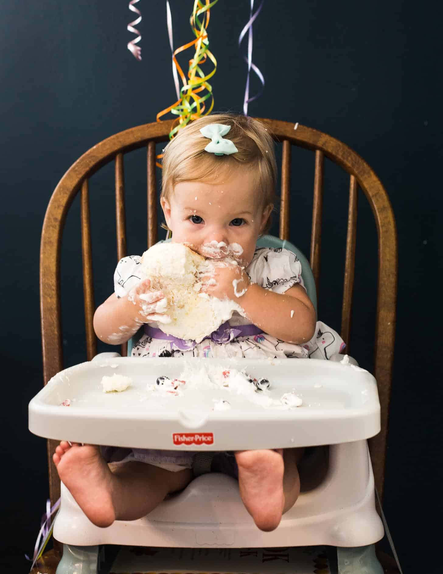 A Baby Girl Eating Cake In A High Chair