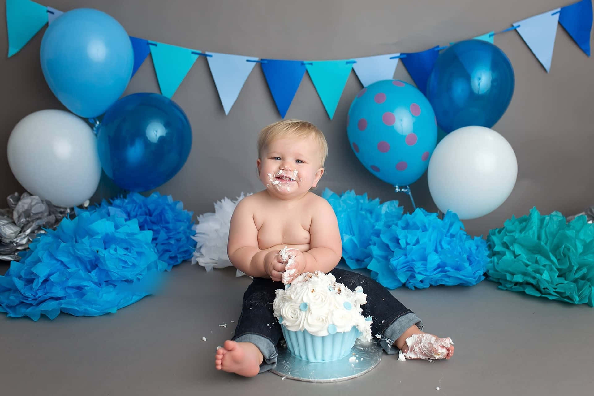 A Baby Boy Sitting In Front Of A Blue And White Cake