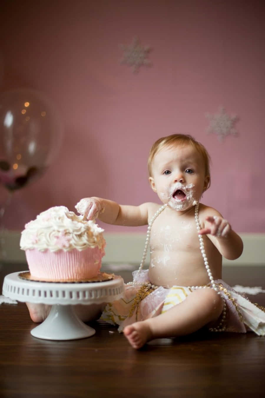 A Baby Girl Is Eating A Cupcake In Front Of A Pink Background