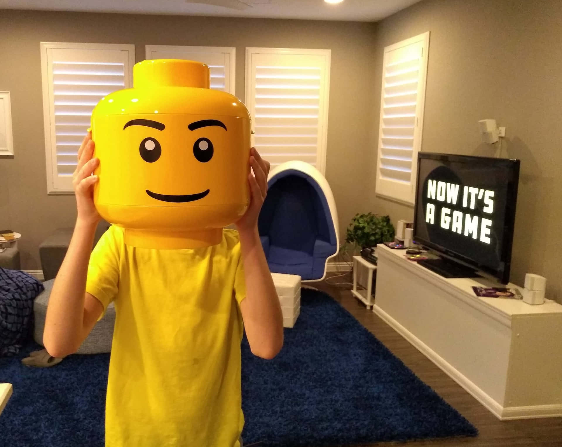A Boy Wearing A Lego Head Mask In A Living Room