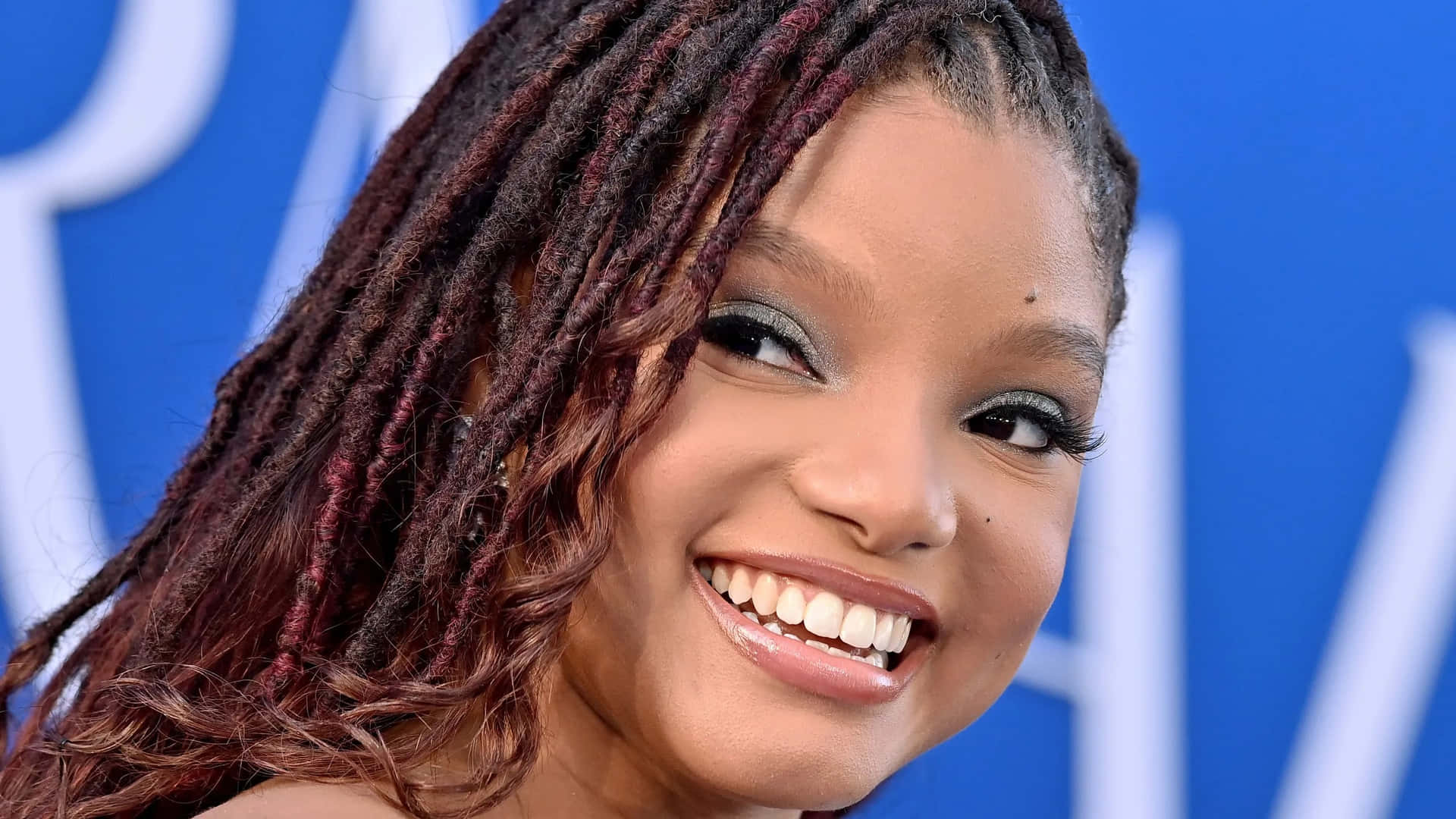 Smiling Celebritywith Braids Blue Backdrop Wallpaper