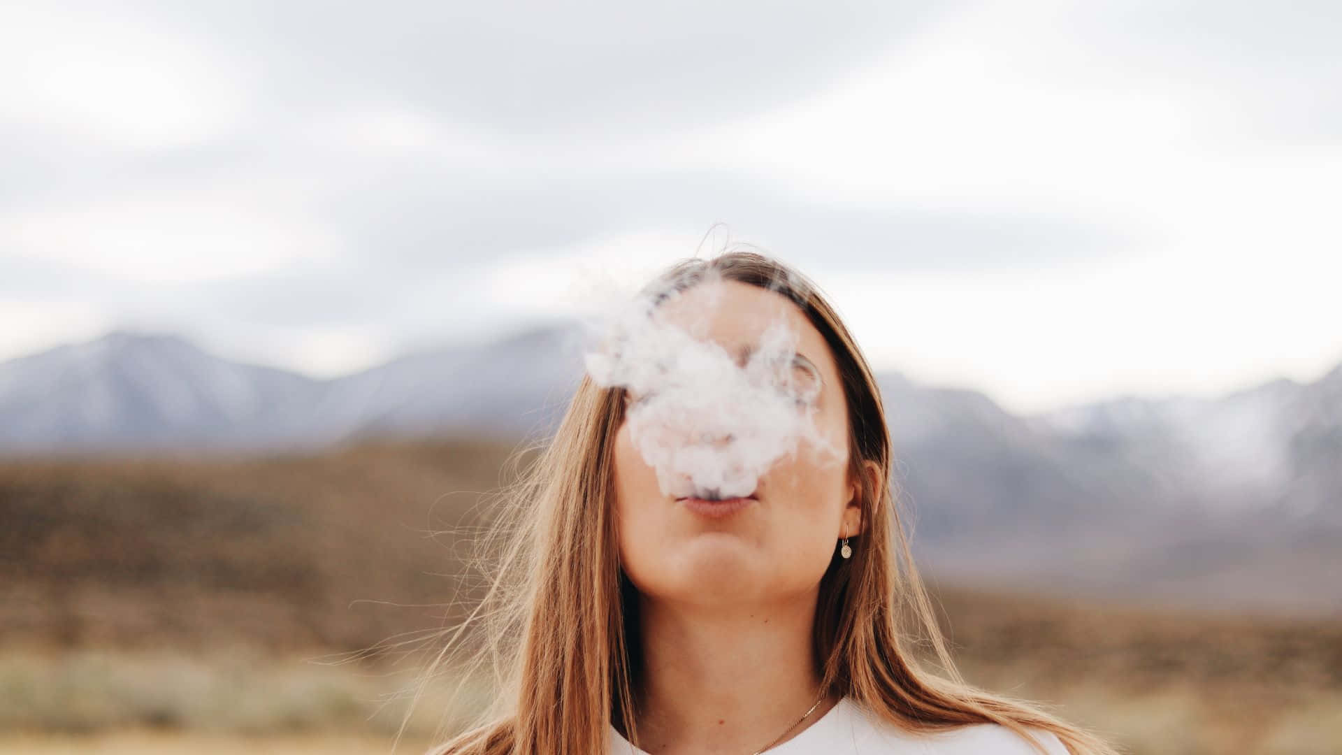 A Woman Smoking A Cigarette In Front Of Mountains
