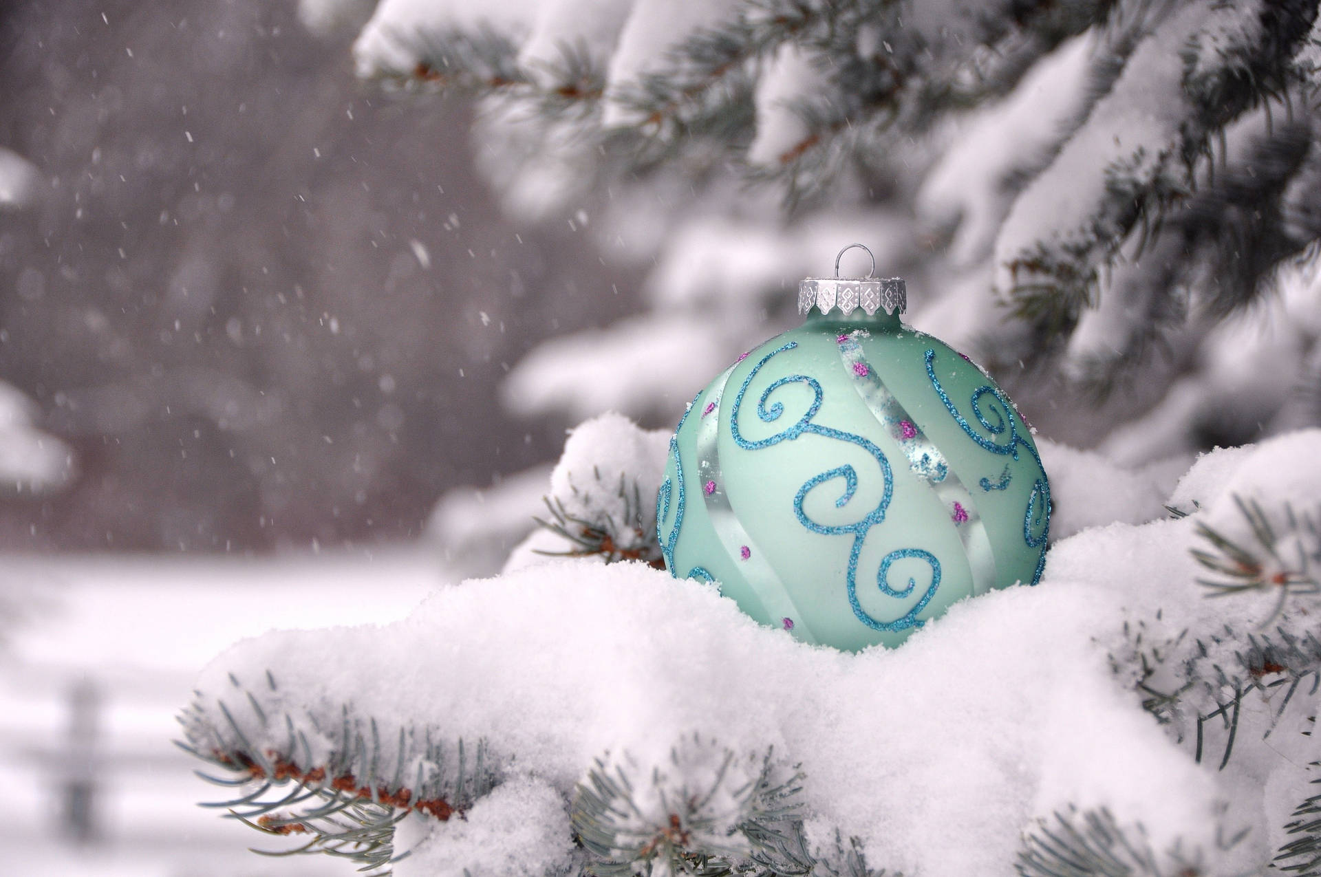 Et blåt ornament siddende på en fyrretræ i sneen. Wallpaper