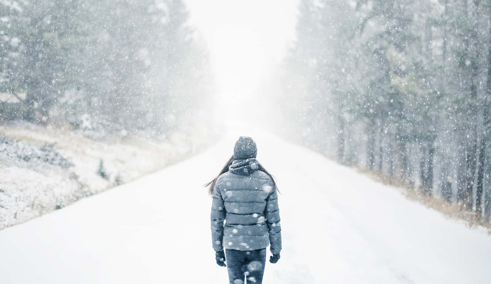 A Woman Walking Down A Snowy Road