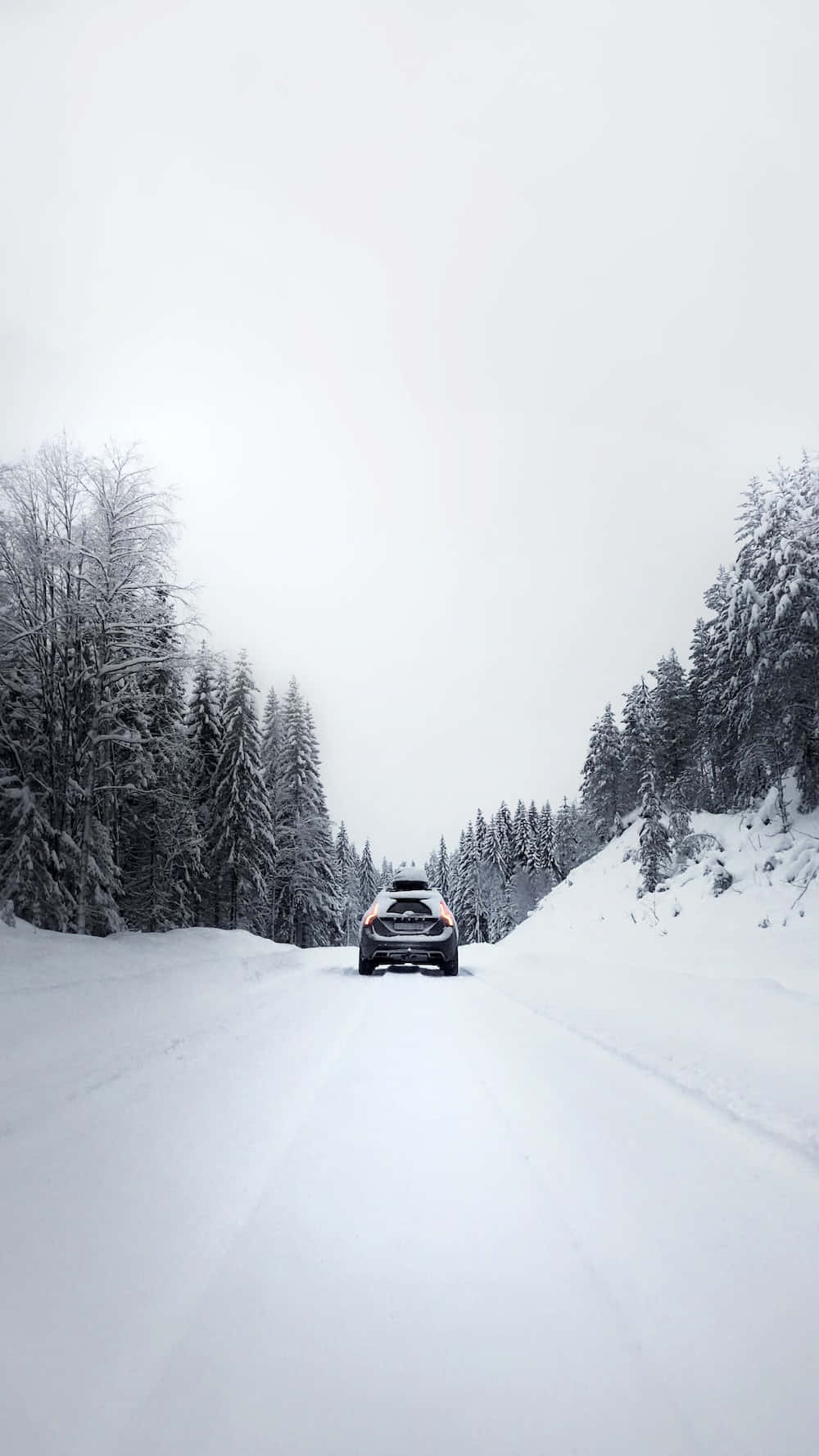 Snow-covered road amidst a serene winter landscape Wallpaper
