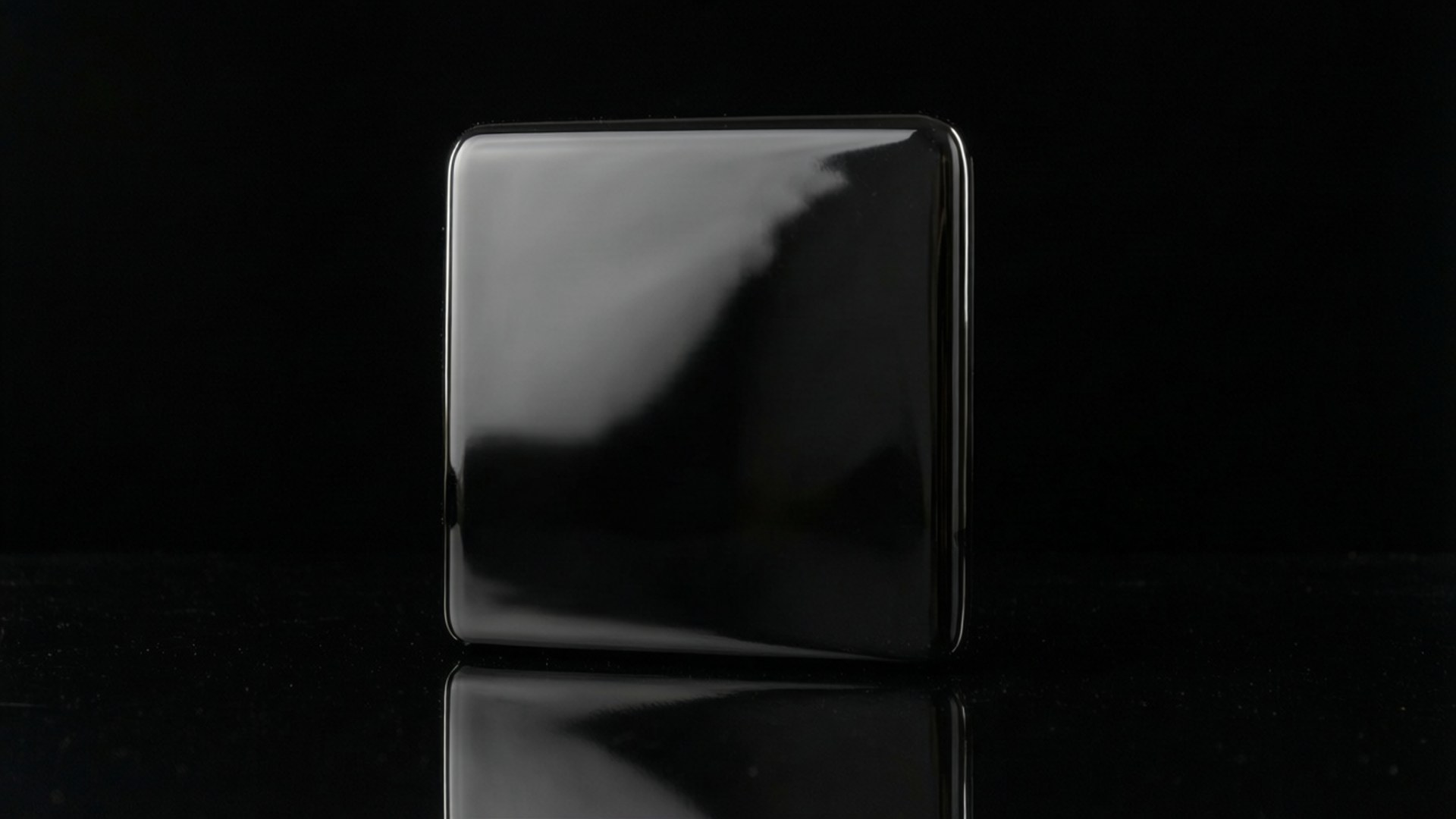 Solid Glossy Black Wallpaper — Objek persegi hitam ramping dengan pantulan mengkilap berdiri di tengah dengan latar belakang hitam murni.