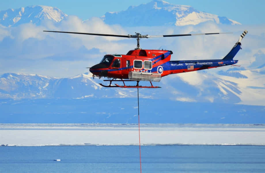 A Helicopter Is Flying Over A Lake With Mountains In The Background
