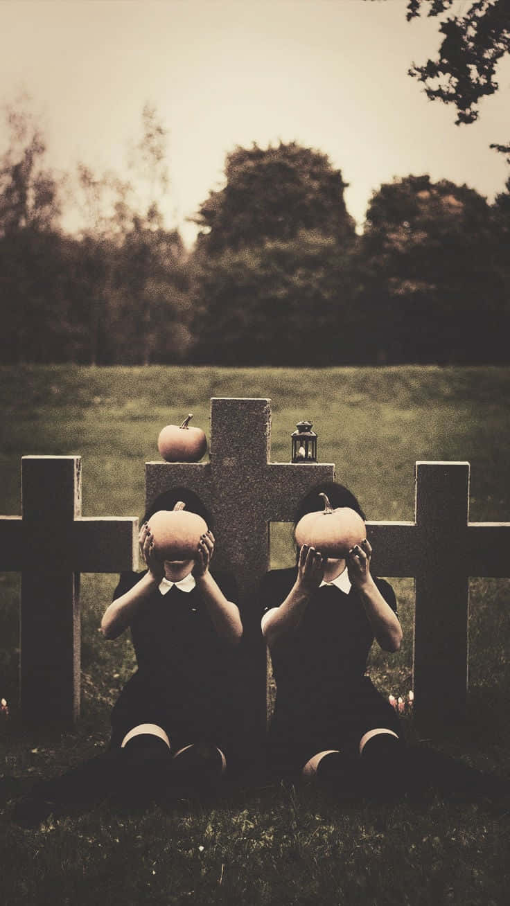 To piger siddende på et gravsted med græskar i deres hænder. Wallpaper