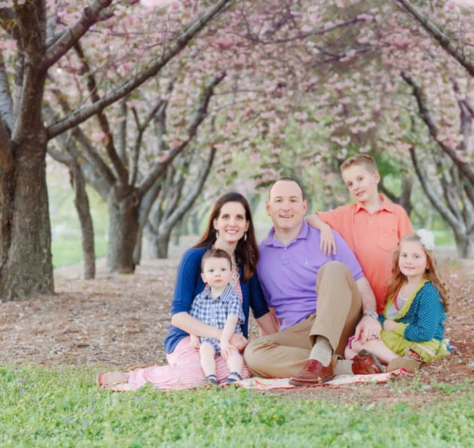 Einefamilie Sitzt Auf Dem Boden Unter Kirschblütenbäumen.