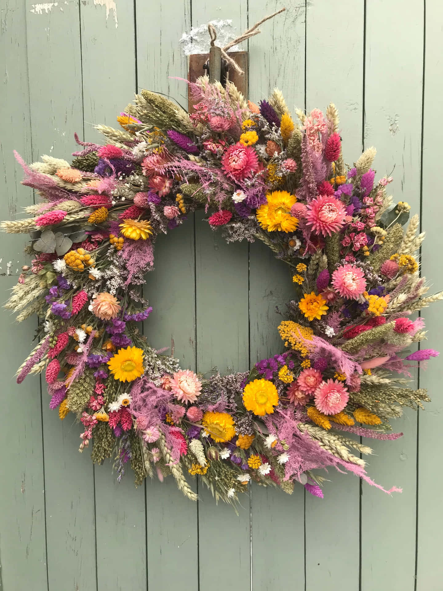 Beautiful Handcrafted Spring Wreath Adorning a Wooden Door Wallpaper