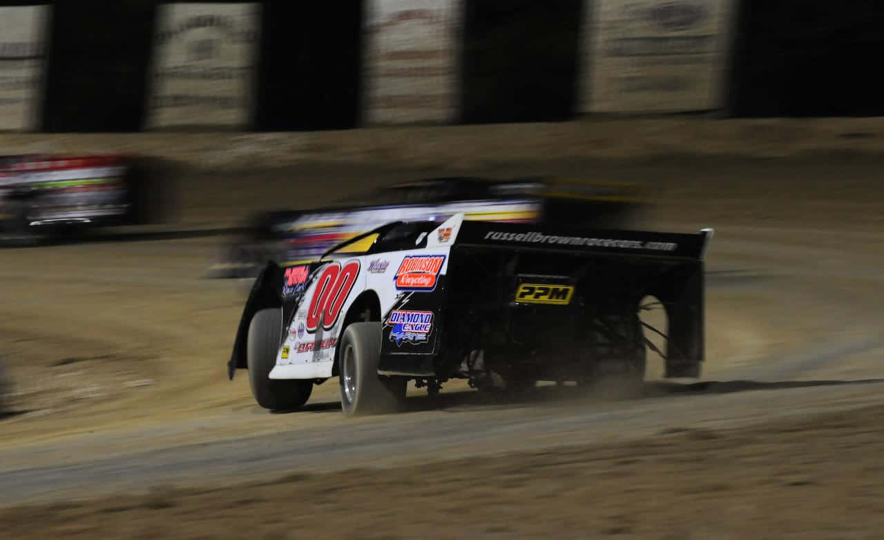 A Dirt Track With Several Cars Racing At Night Wallpaper