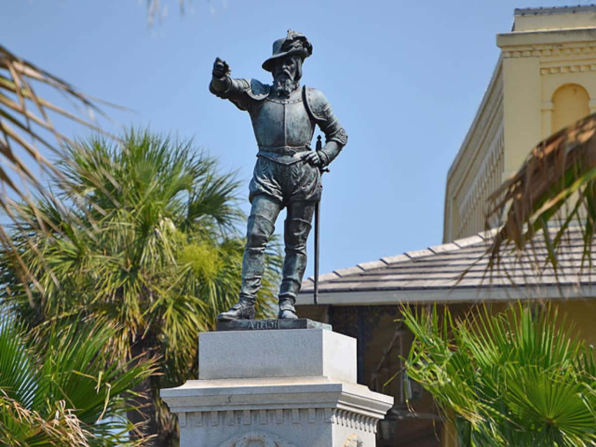 A Statue Of A Man With A Gun In Front Of Palm Trees