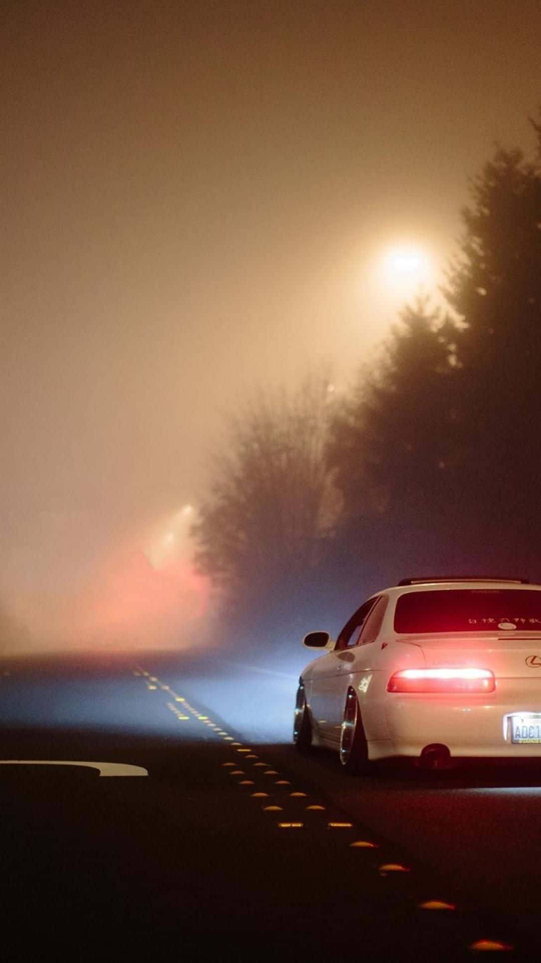 Einweißes Auto Fährt Auf Einer Nebligen Straße Bei Nacht. Wallpaper