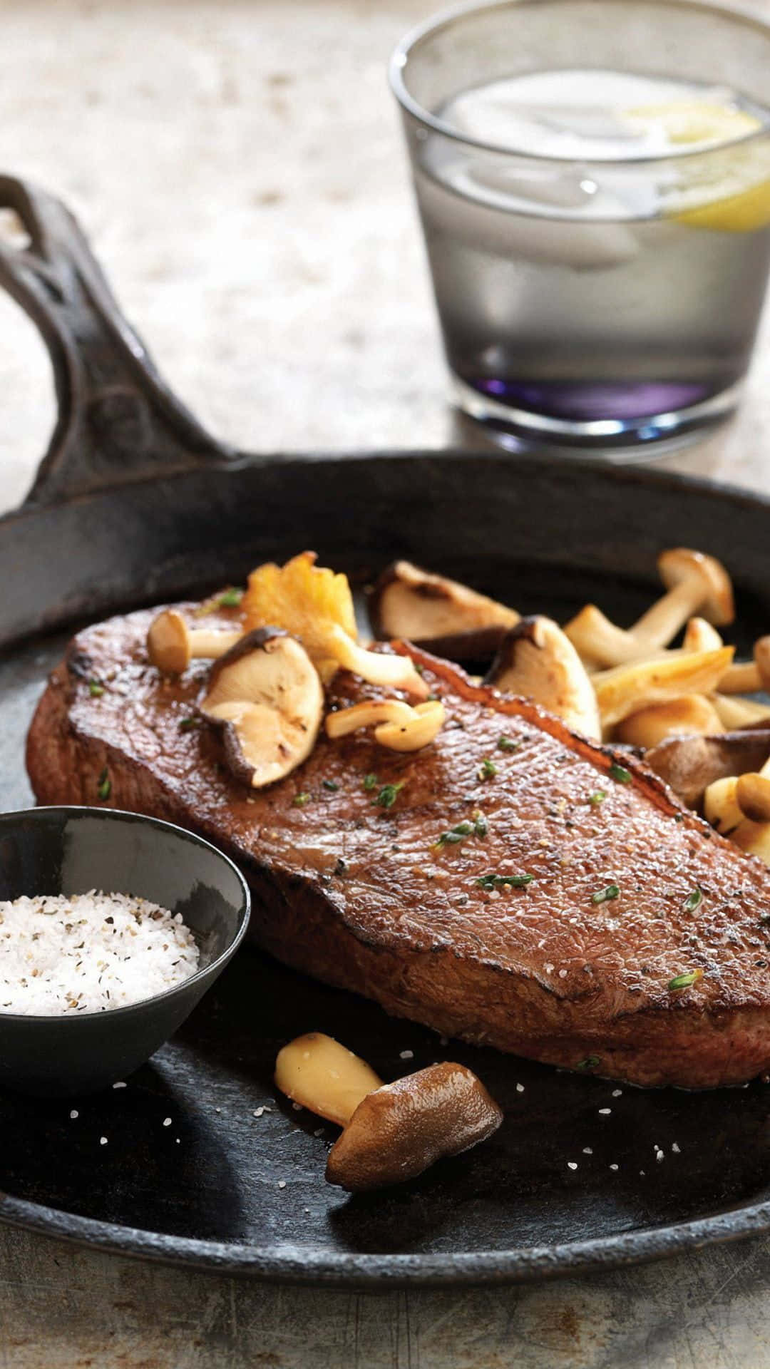 A Steak On A Skillet With Mushrooms And A Glass Of Wine