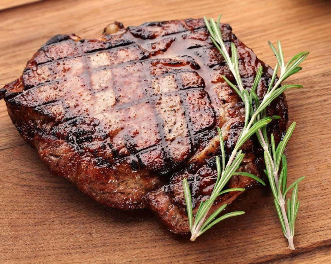 A Steak With Rosemary On A Wooden Table