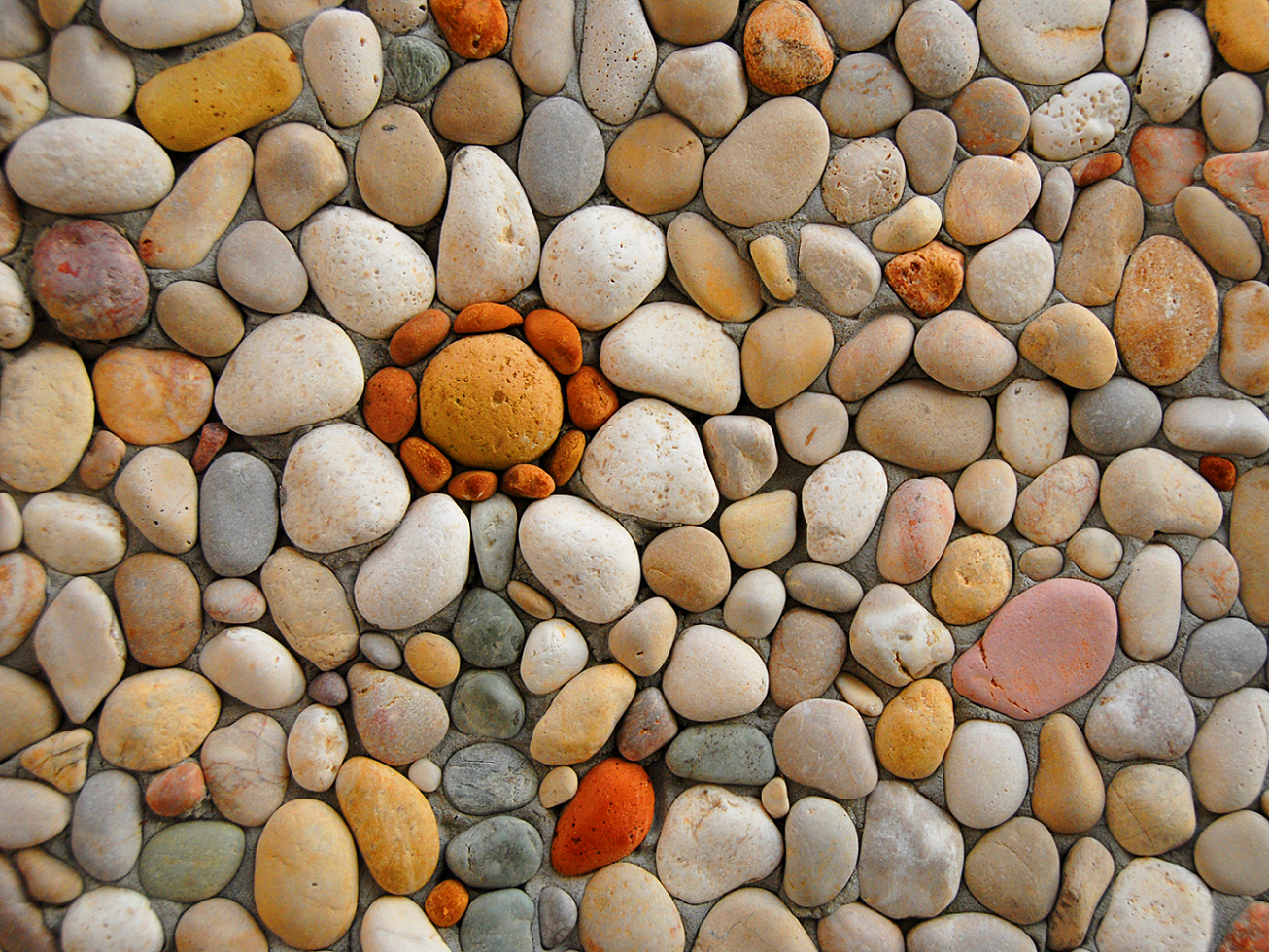 Ancient stone wall in a field Background — A mosaic of smooth rounded stones in earthy tones arranged in a sunburst pattern with a central orange stone.