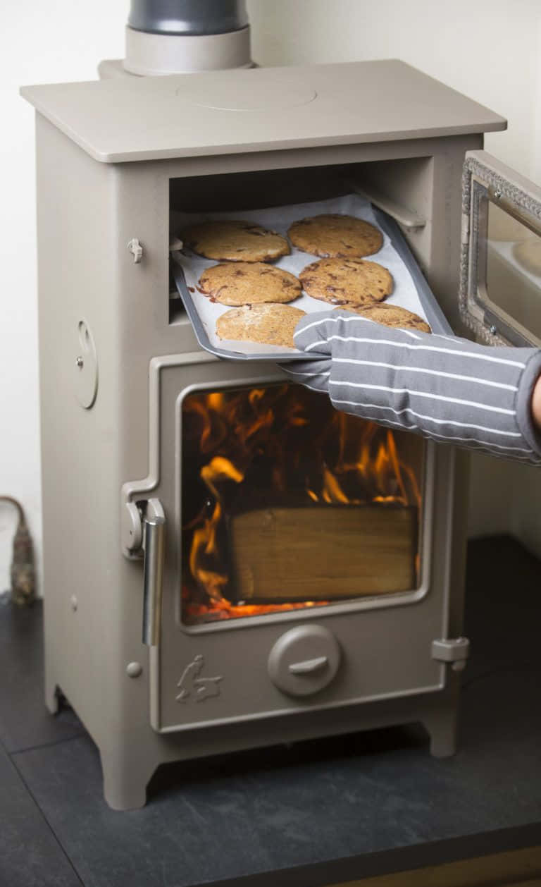 A Woman Is Putting Cookies Into A Wood Burning Stove