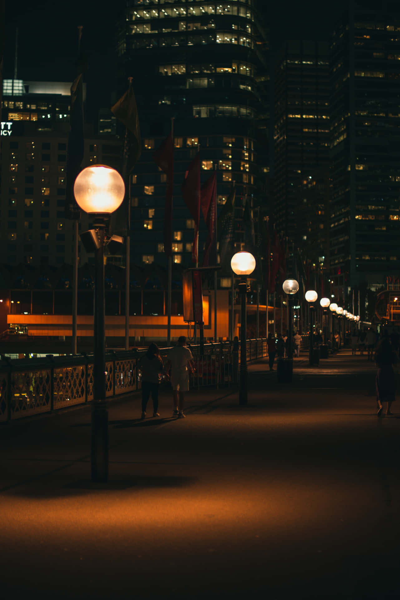 A City At Night With People Walking Along The Sidewalk Wallpaper