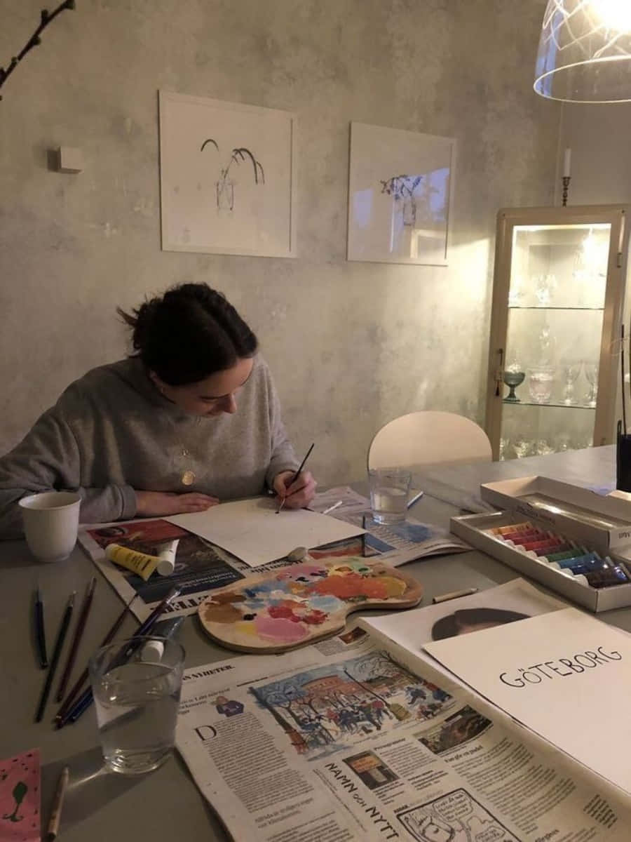 A Woman Is Sitting At A Table With Paints And Brushes