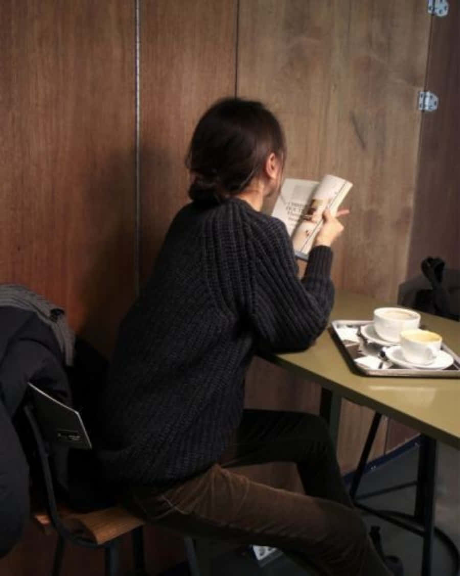 A Woman Reading A Book At A Table