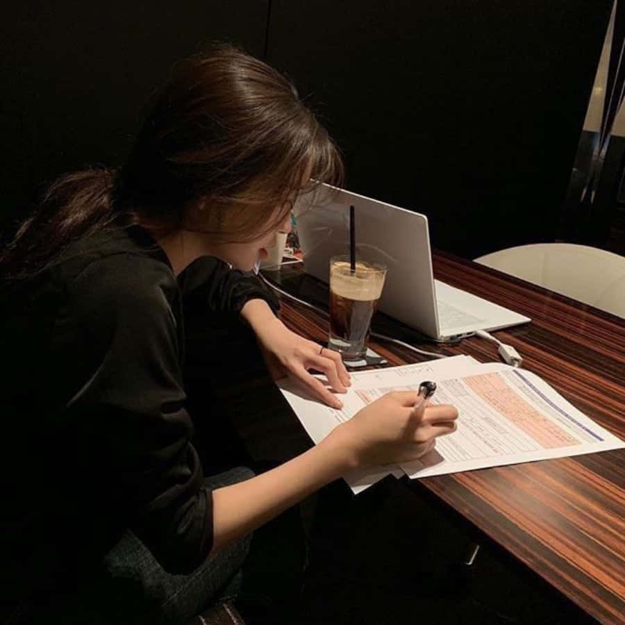 A Woman Is Sitting At A Table With A Laptop And A Cup Of Coffee