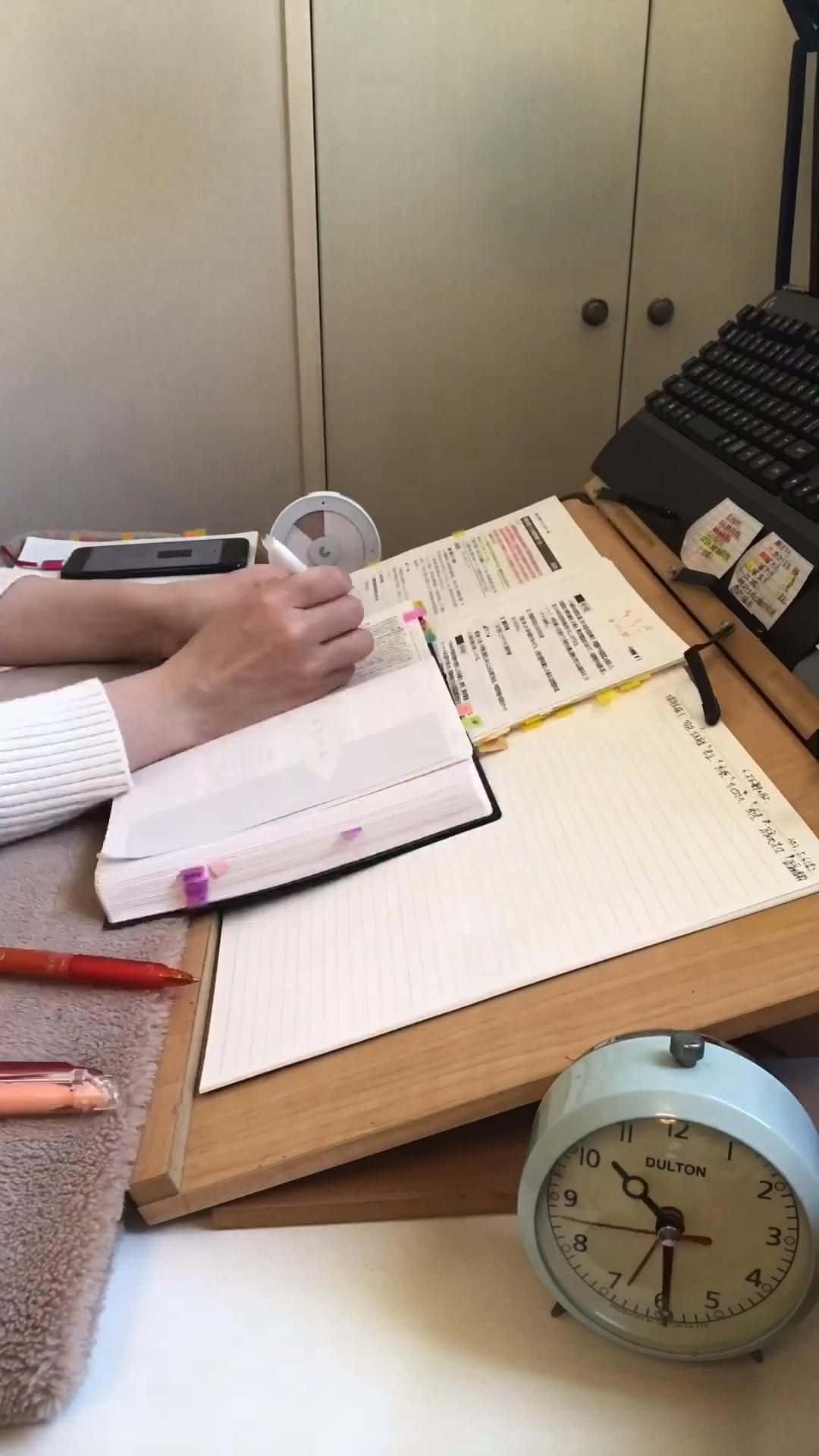 A Woman Is Sitting At Her Desk With A Notebook And A Clock